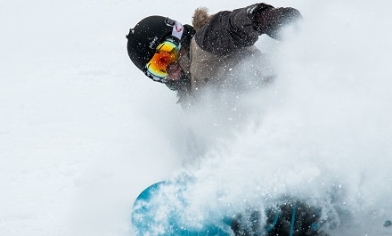 Person snowboarding through snow surrounded with snow spray